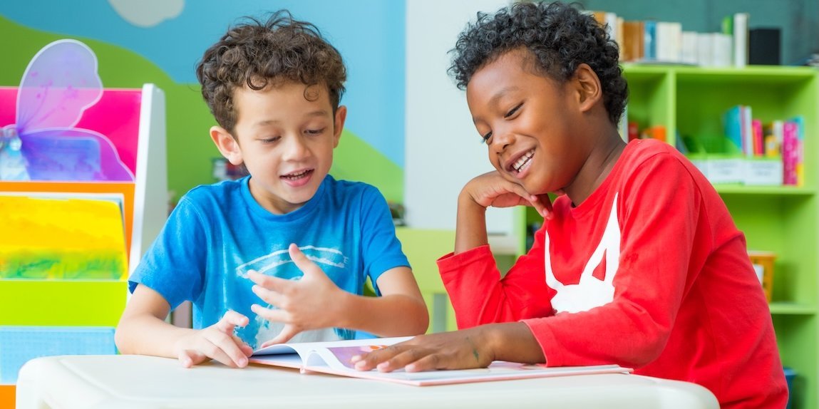 Zwei Jungen in einer Kita sitzen am Tisch und schauen sich ein Buch an.
