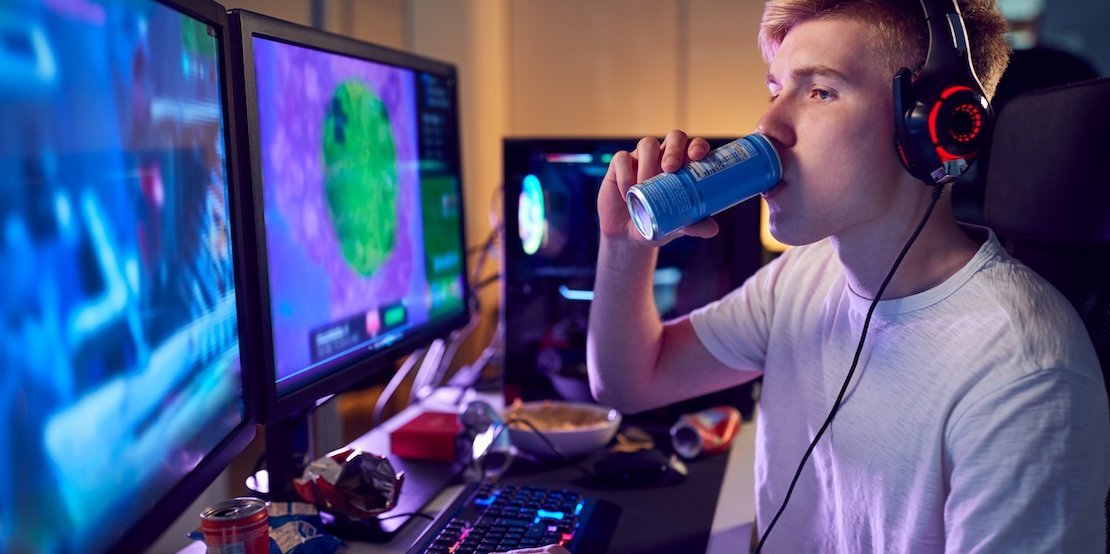 Junger Gamer sitzt am PC und trinkt einen Energydrink.. Artikel "Energydrinks" öffnen.