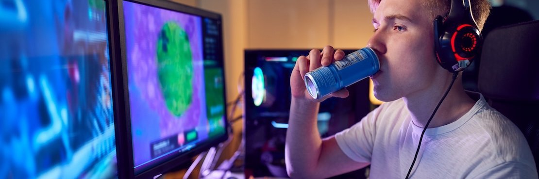 Junger Gamer sitzt am PC und trinkt einen Energydrink.
