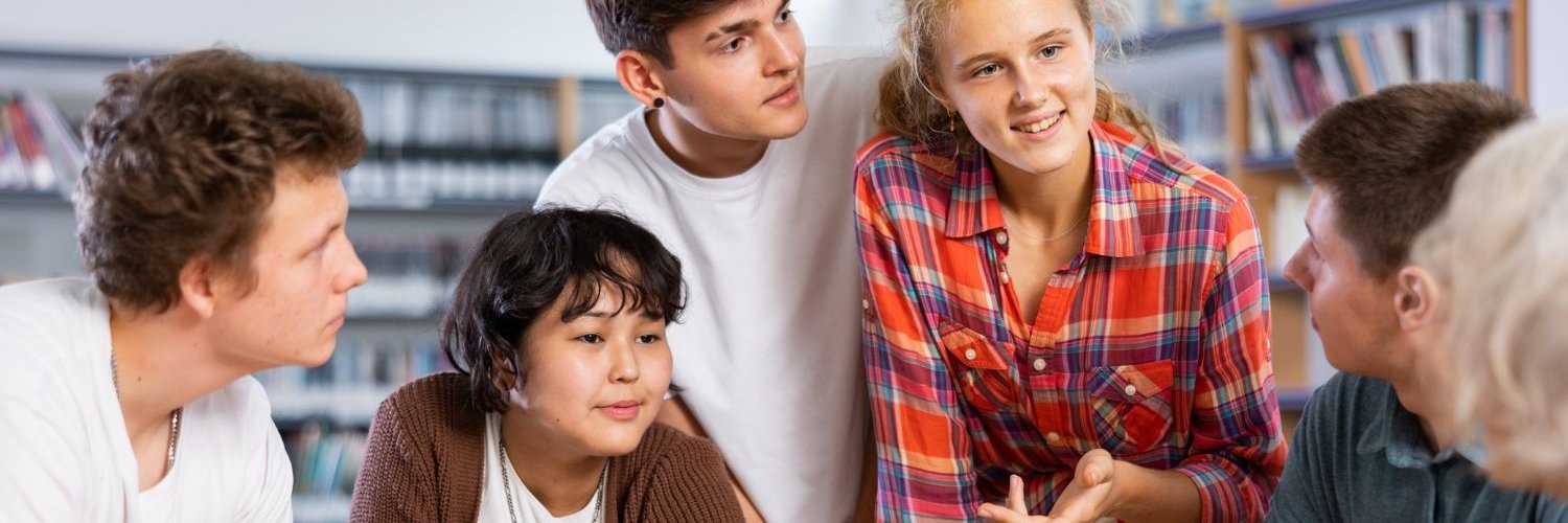 Eine Gruppe von Schülerinnen und Schülern verschiedenster Nationalitäten diskutiert an einem Tisch. 