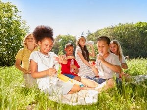 Eine Gruppe Kinder mit Wasserflaschen in der Hand sitzen auf einer sommerlichen Wiese.