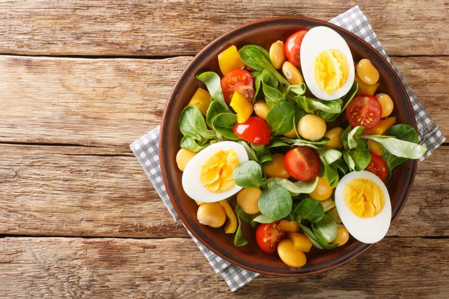 Auf einem Teller liegt Salat mit Tomaten, Eiern und Süßlupinen.