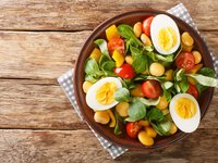 Auf einem Teller liegt Salat mit Tomaten, Eiern und Süßlupinen.