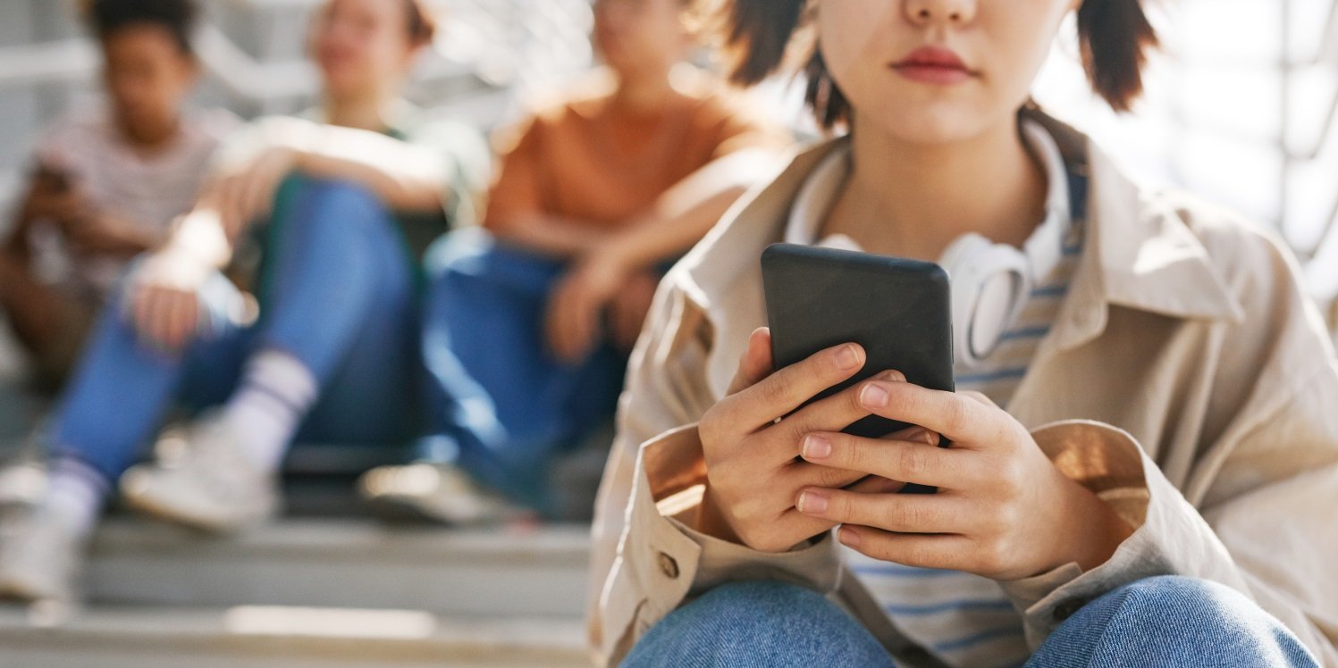 Ein junges Mädchen sitzt auf einer Treppe und schaut auf ihr Smartphone. Im Hintergrund sitzen weitere Mädchen.. Artikel "Starker Anstieg von Essstörungen bei jungen Mädchen" öffnen.