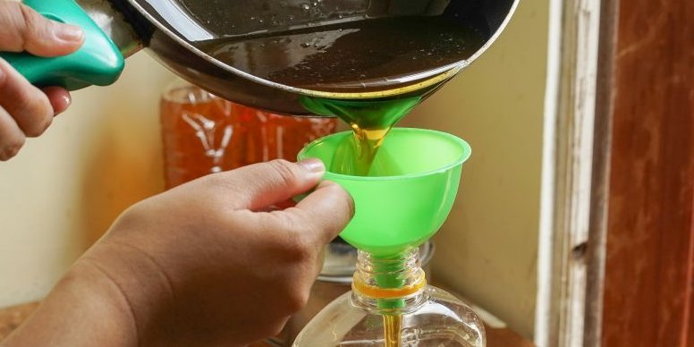 Mithilfe eines Trichters wird benutztes Rapsöl aus einer Bratpfanne in eine Plastikflasche gegossen. Das verwendete Rapsöl ist dunkelgelb bis bernsteinfarbig.