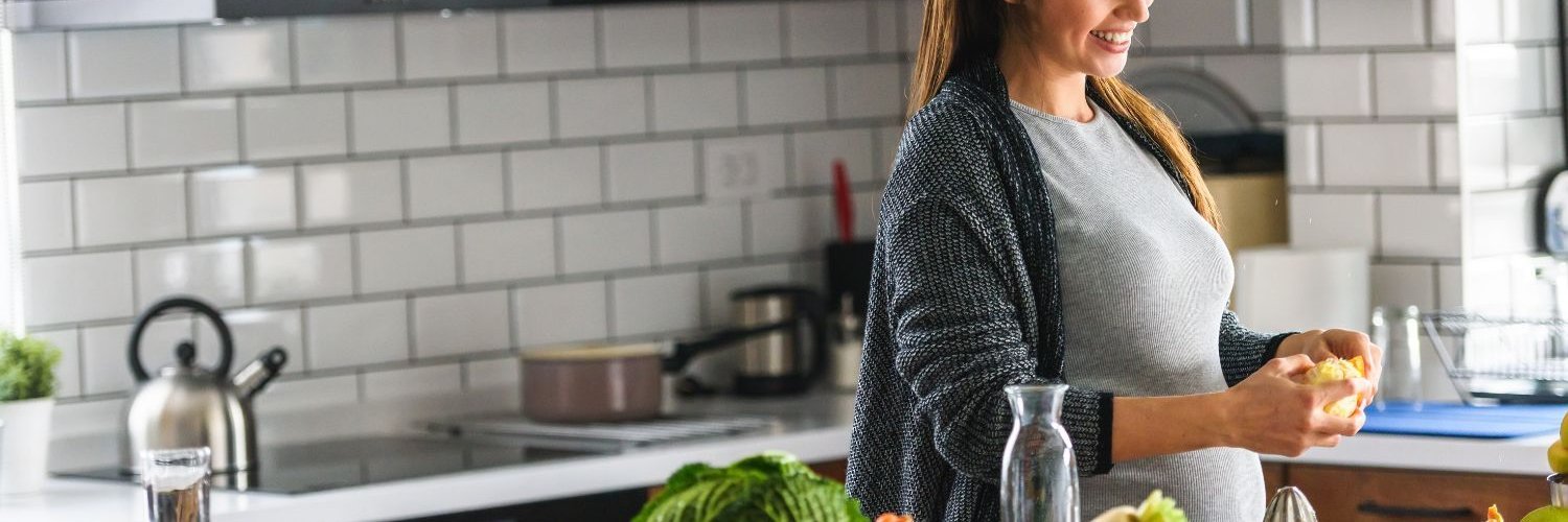 Eine schwangere Frau bereitet in ihrer Küche zu Hause gesundes Essen mit viel Obst und Gemüse zu.
