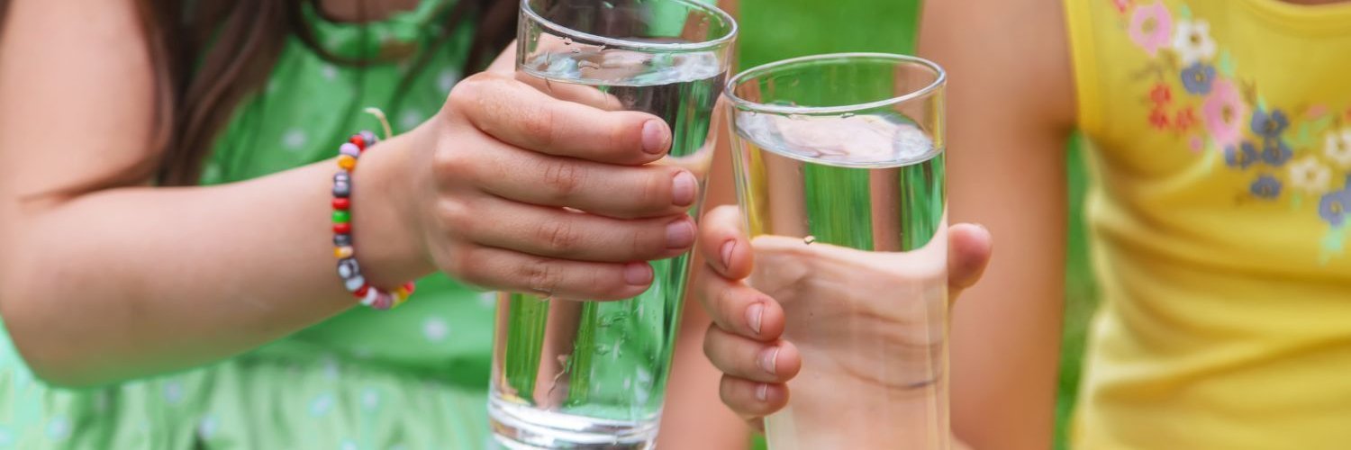 Zwei Mädchen stoßen mit zwei vollen Wassergläsern miteinander an.