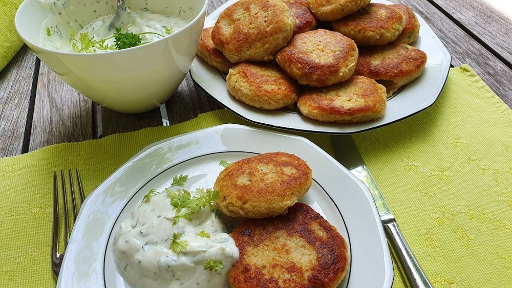 Mehrere vegetarische Bratlinge liegen auf einem Teller mit Kräuterquark und in einer Schüssel.