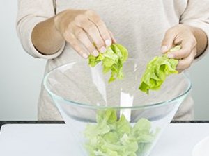 Eine Person gibt Salatblätter in eine Glasschüssel.