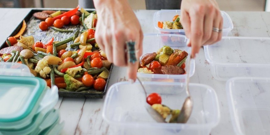 Auf einem Backblech liegt buntes Ofengemüse. Hände füllen dieses mit zwei Löffeln in Kunststoffdosen. . Artikel "Mealprep für die Mittagspause" öffnen.