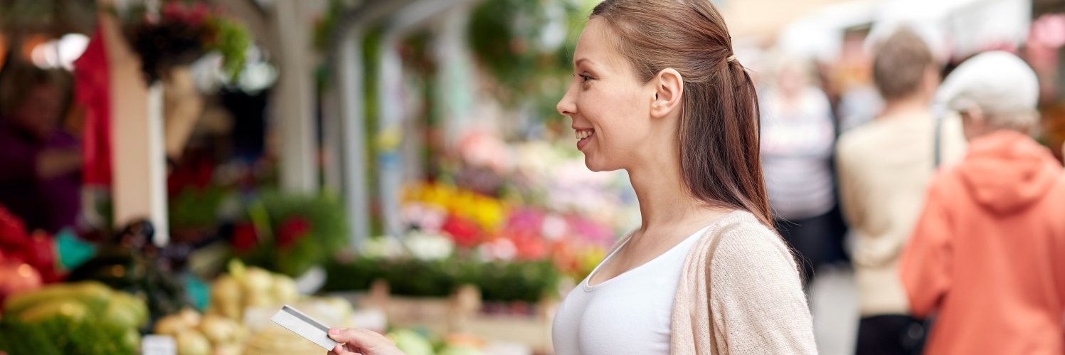 Eine Frau kauft an einem Marktstand Obst und Gemüse ein.