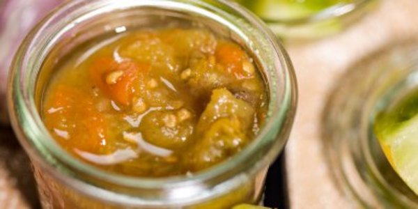 Ein kleines Glas Tomaten-Chutney steht neben grünen Tomatenstücken.