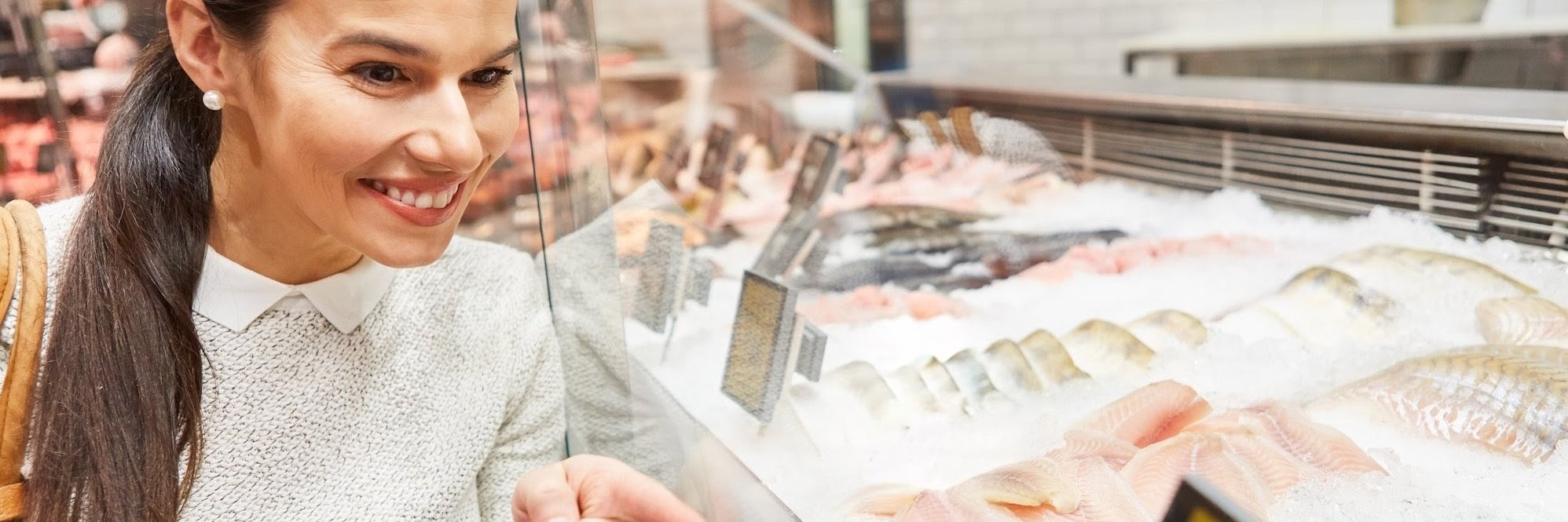 Eine Frau steht an einer Theke mit frischem Fisch und zeigt mit dem Finger darauf.