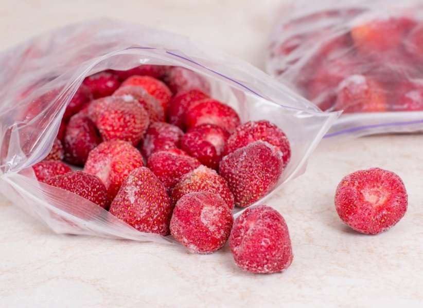 Einzelne, gefrorene Erdbeeren liegen in einer geöffneten Gefriertüte.