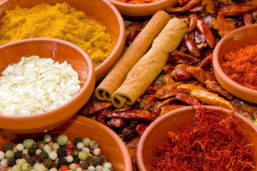 Auf einem Tisch liegen viele verschiedene Gewürze wie Zimt-Stangen, Chili-Schoten, Pfefferkörner, Lorbeer und Orangenschalen.