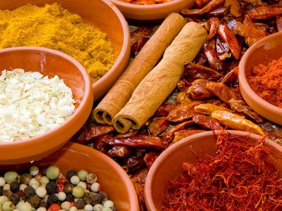 Auf einem Tisch liegen viele verschiedene Gewürze wie Zimt-Stangen, Chili-Schoten, Pfefferkörner, Lorbeer und Orangenschalen.