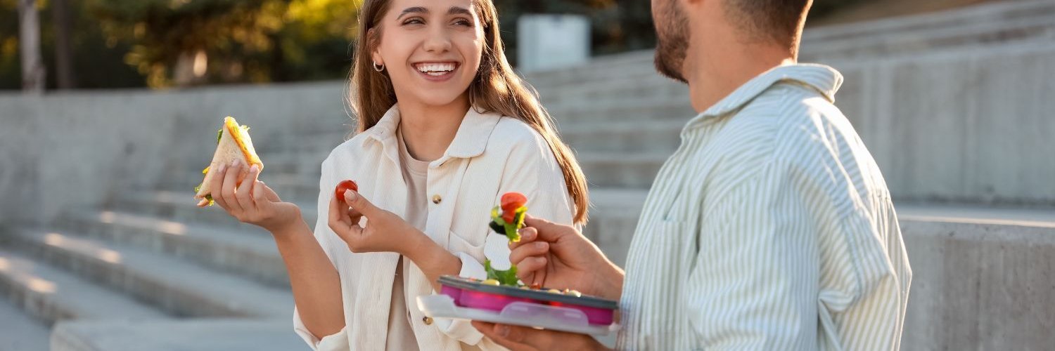 Eine junge Frau und ein junger Mann essen ihr Mittagessen im Freien.