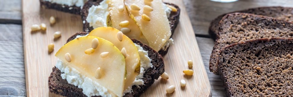 Belegtes Schwarzbrot auf einem Brettchen und Schwarzbrotscheiben daneben liegend.