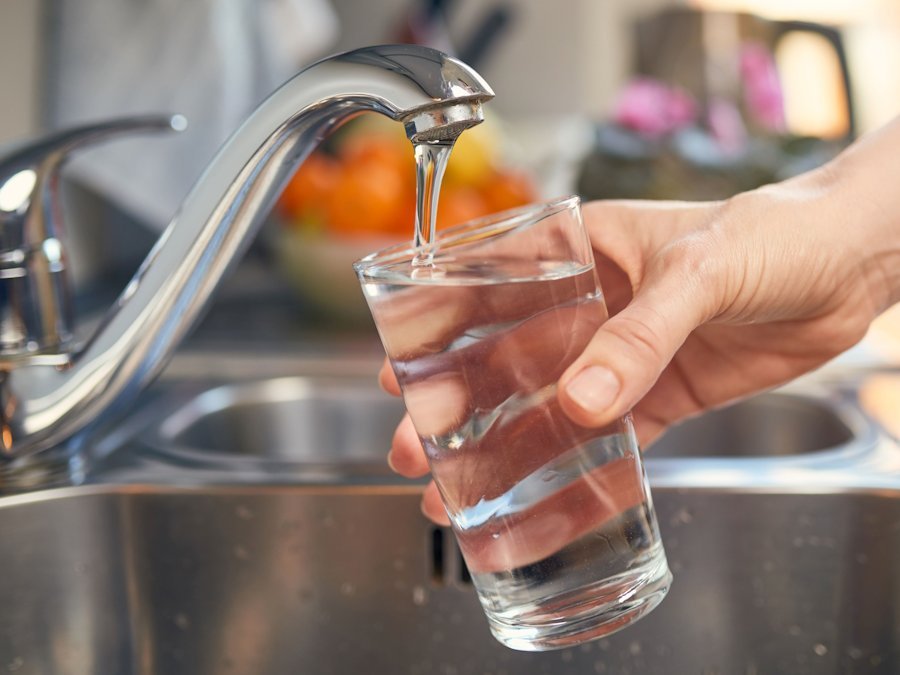 Eine Hand hält ein Glas unter einen Wasserhahn, aus dem Trinkwasser fließt. 