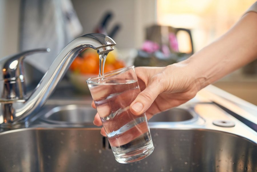 Eine Hand hält ein Glas unter einen Wasserhahn, aus dem Trinkwasser fließt. 