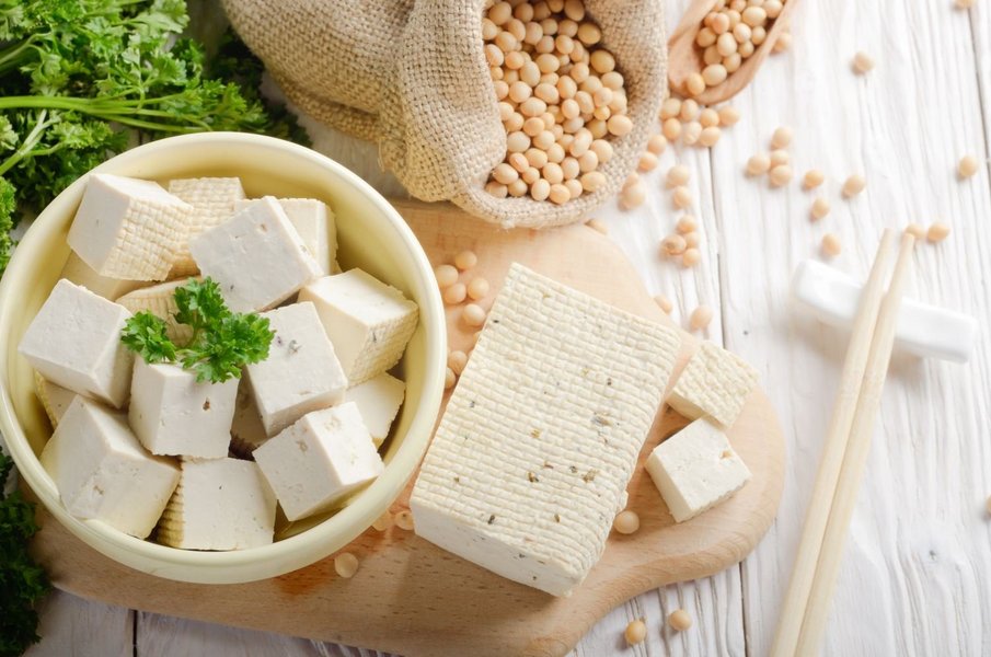 Abgebildet sind gewürfelter Tofu in einer Schüssel und daneben liegen lose Sojabohnen.