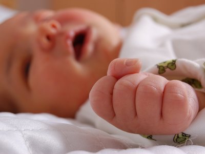 Ein Baby liegt auf dem Rücken mit geöffnetem Mund und einer geballten Faust.