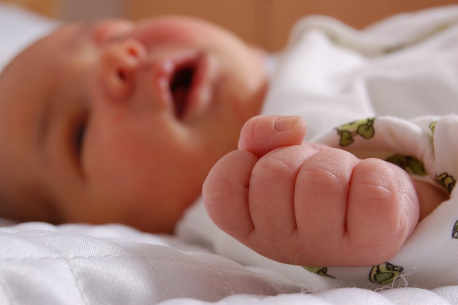 Ein Baby liegt auf dem Rücken mit geöffnetem Mund und einer geballten Faust.