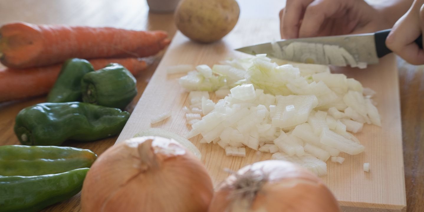 Eine Frau schneidet Zwiebeln auf einem Holzbrett. Artikel "How-to: Obst und Gemüse" öffnen.