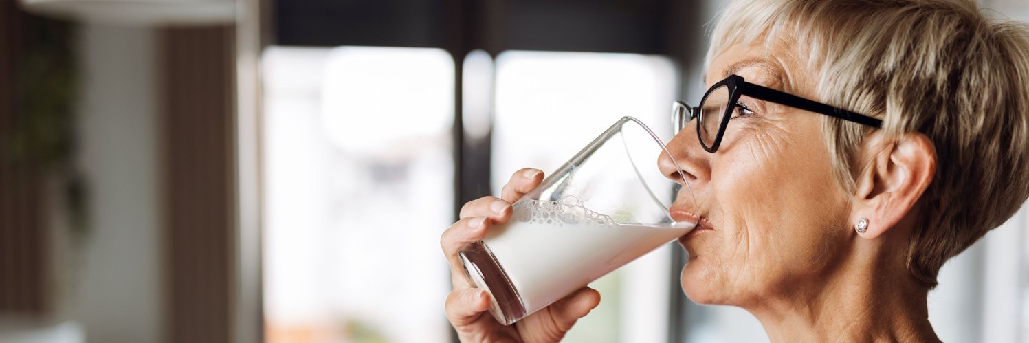 Eine ältere Frau mit grauen kurzen Haaren trinkt aus einem Glas Milch.