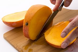 Mango wird mit einem Messer entlang des Kerns ein drei Teile geschnitten