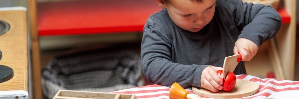 Ein Junge spielt mit Holzmesser und Holzgemüse.