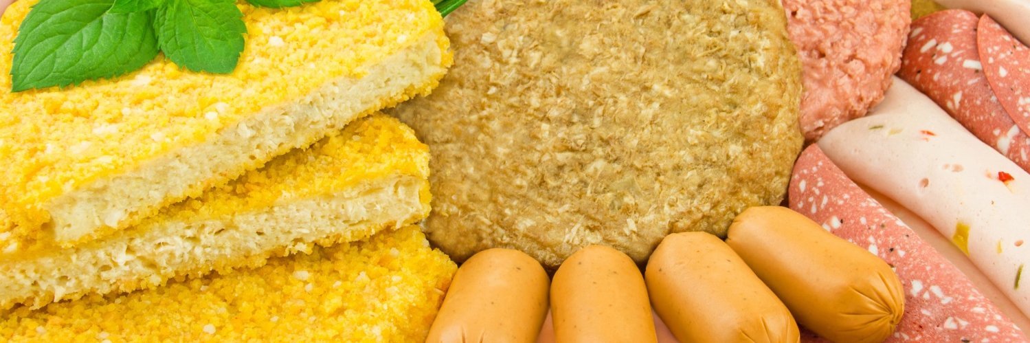 Eine Fläche ist bedeckt mit verschiedenen pflanzliche Patties, Aufschnittsorten und Aufstrich in Wurstform, dekoriert mit Basilikumblättern und Rosmarin.