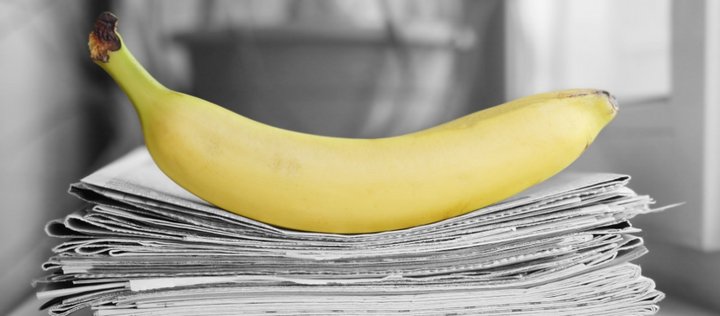 Eine gelbe Banane liegt auf gestapelten Zeitungen.