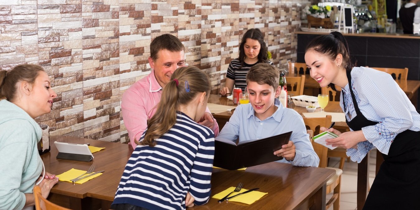 Kinder sitzen an einem Restaurant-Tisch und werden bedient.. Artikel "Unser Restaurant-Tisch" öffnen.