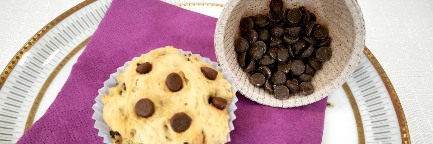 Auf einem Teller liegt ein Muffin mit Stückchen einer Schokoladenalternative ohne Kakao. 