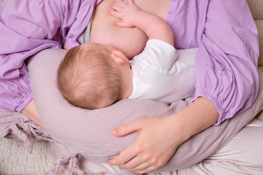 Ein Baby liegt auf einem Stillkissen und wird an der Brust gestillt.