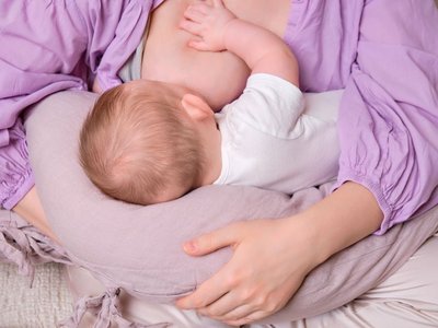 Ein Baby liegt auf einem Stillkissen und wird an der Brust gestillt.