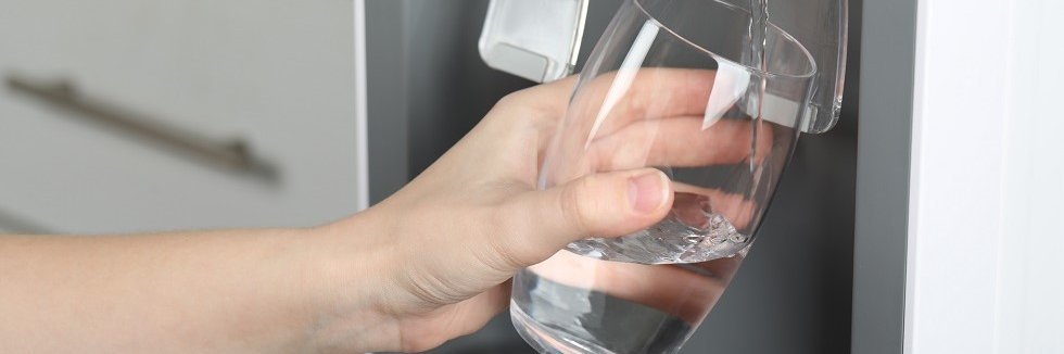 Ein Glas wird mit Wasser aus einem Wasserspender gefüllt.