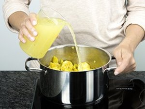 Eine Person gießt Gemüsebrühe in einen Topf.