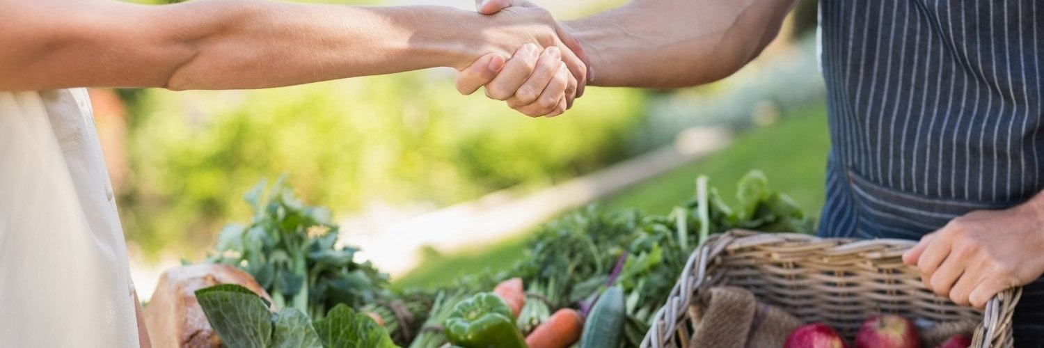 An einem Obst- und Gemüsestand reichen sich zwei Menschen die Hand. 