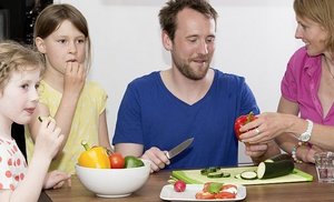 Zwei Mädchen, Mann und Frau essen am Tisch Gemüse