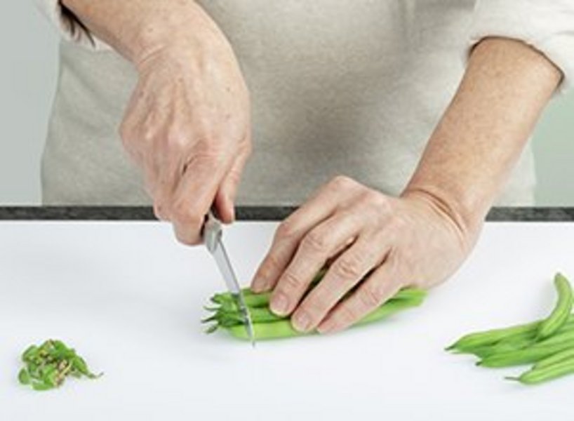 Person schneidet mit einem kleinen Messer die Stengel von Bohnen ab