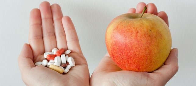 In einer Hand sind Medikamente und in der anderen Hand ein Apfel