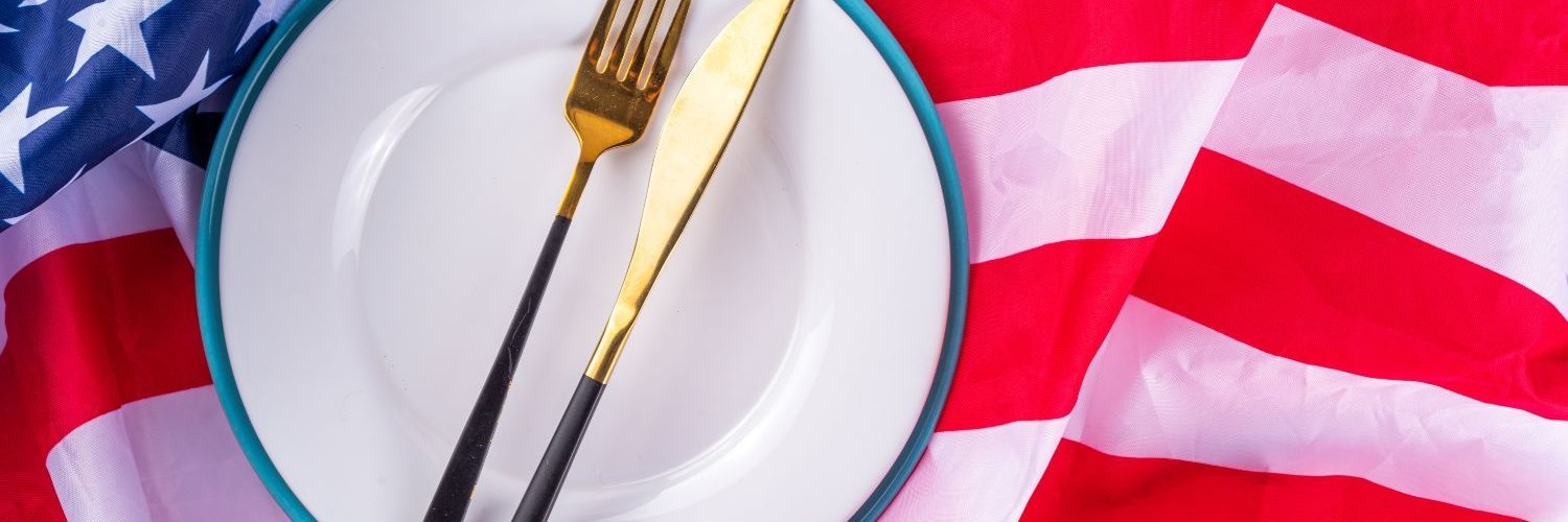 Auf einer US-amerikanischen Flagge liegt ein weißer Teller mit Messer und Gabel.