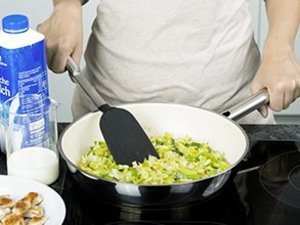 Eine Person vermischt Lauch und Hähnchen in Pfanne.