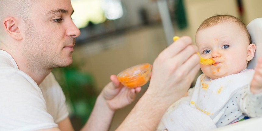 Ein Vater füttert sein Baby mit Brei. . Artikel "Babys erster Brei" öffnen.