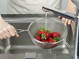 Eine Person wäscht Erdbeeren im Sieb.