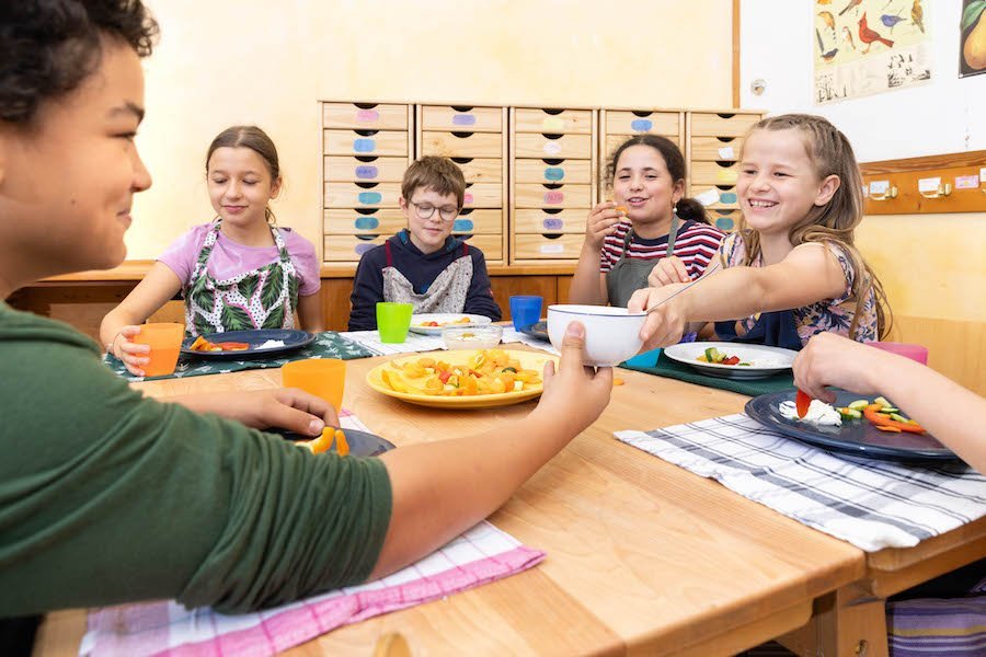 Schüler sitzen am Tisch im Klassenzimmer und essen selbst geschnippeltes Knabbergemüse.