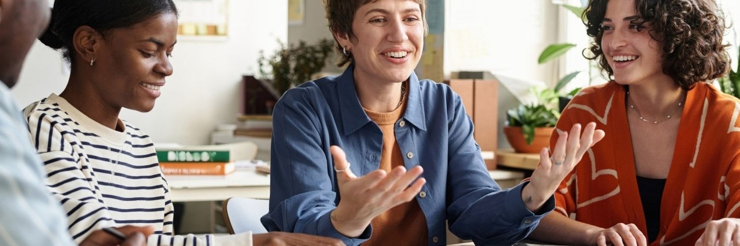 Drei junge Frauen sitzen an einem Tisch mit aufgeschlagenen Büchern und diskutieren.