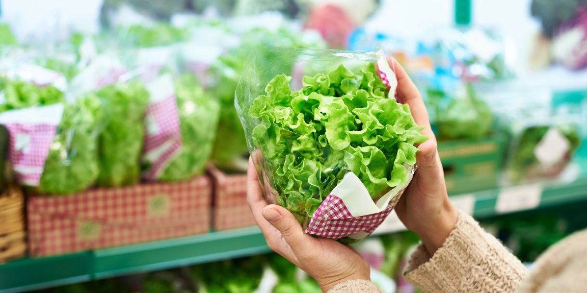 Frau hält einen Lollo bionda vor einem Supermarktregal in der Hand.. Artikel "Salate: Von der Ernte in den Handel" öffnen.